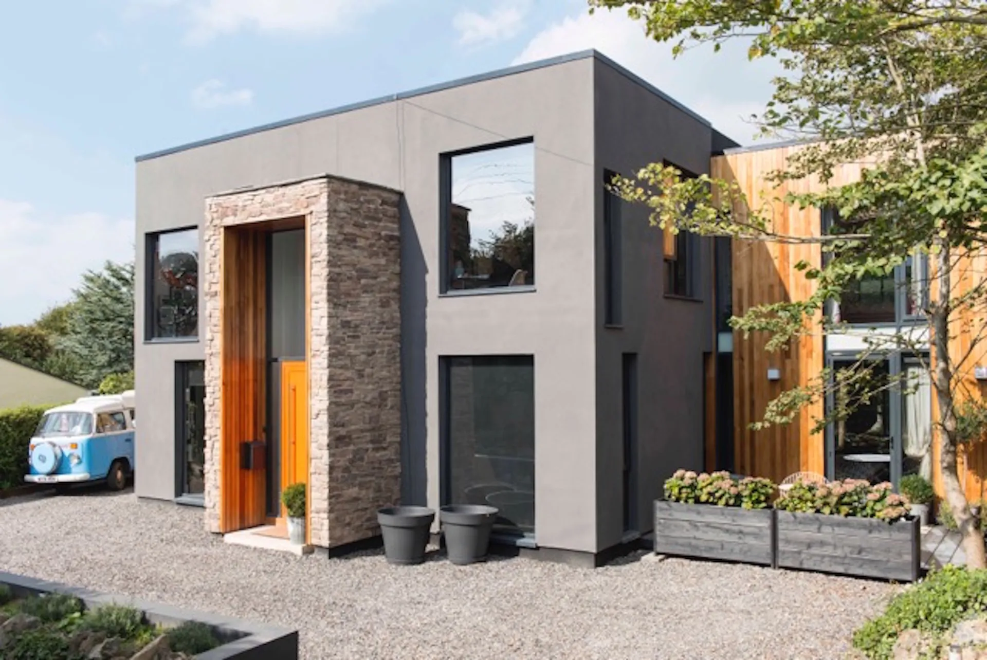 Building frontage with stone clad entrance feature, dark grey rendered central section and timber clad side cubes.