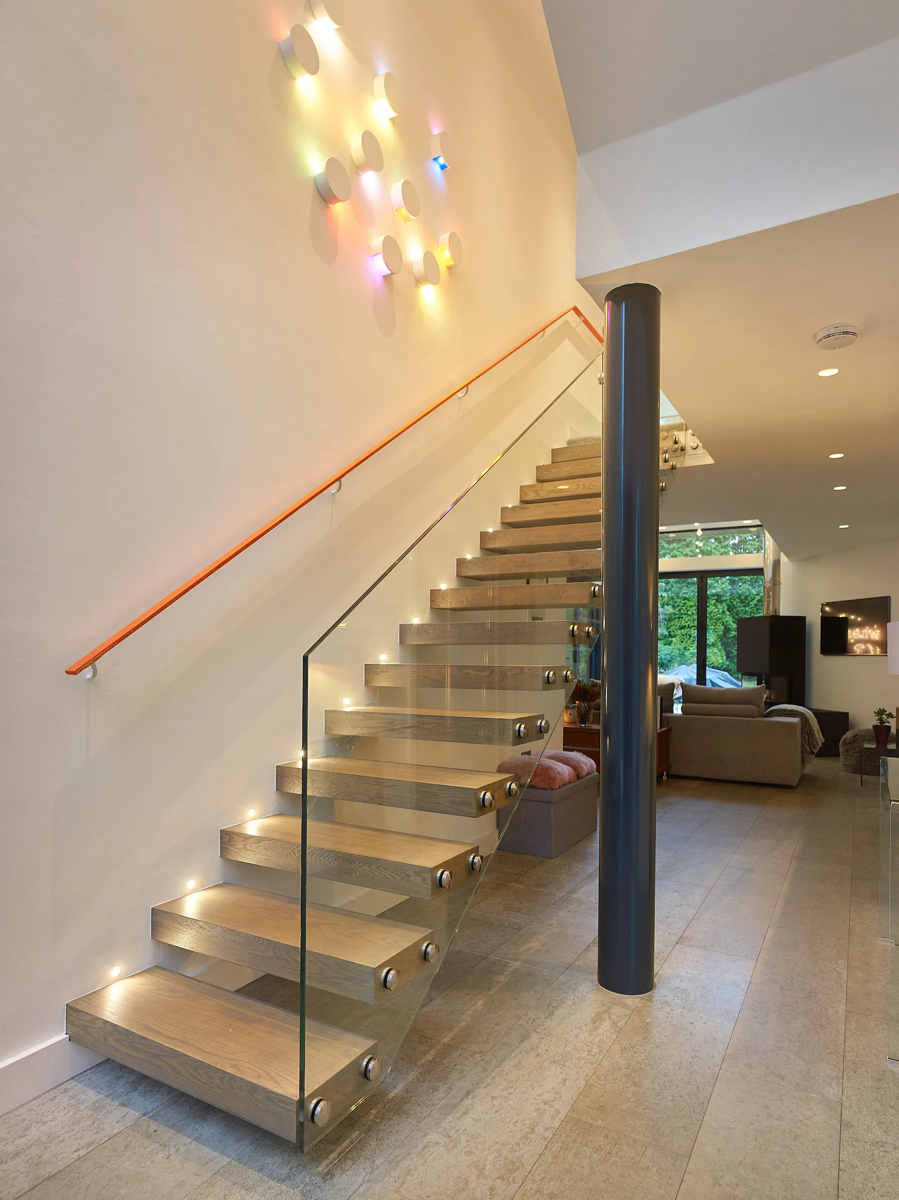 Double height entrance hall featuring cantilevered stairs and glass balustrade, linking with lounge