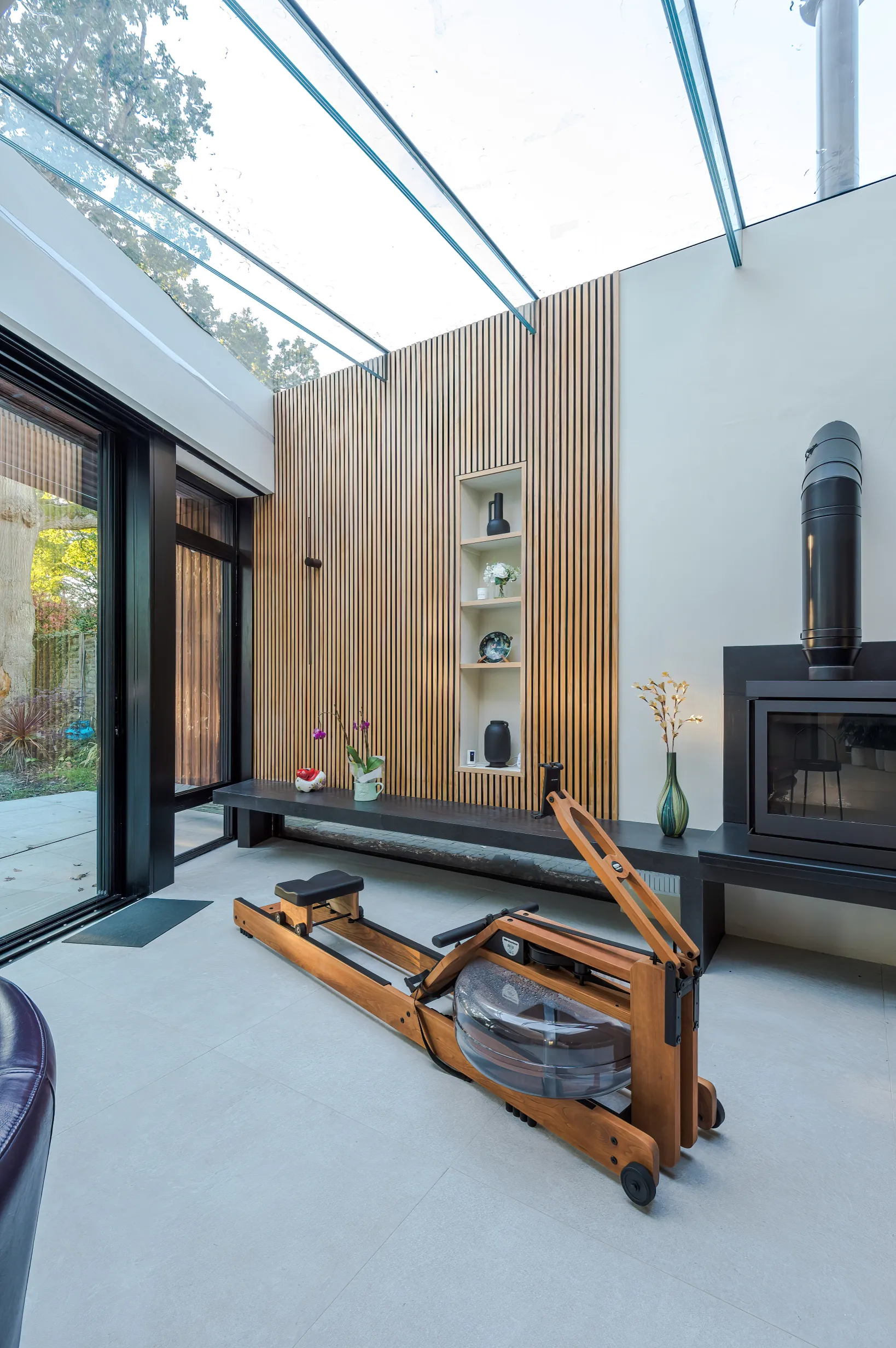 View of exercise zone featuring glass roof, log burner and floating, timber-clad wall.