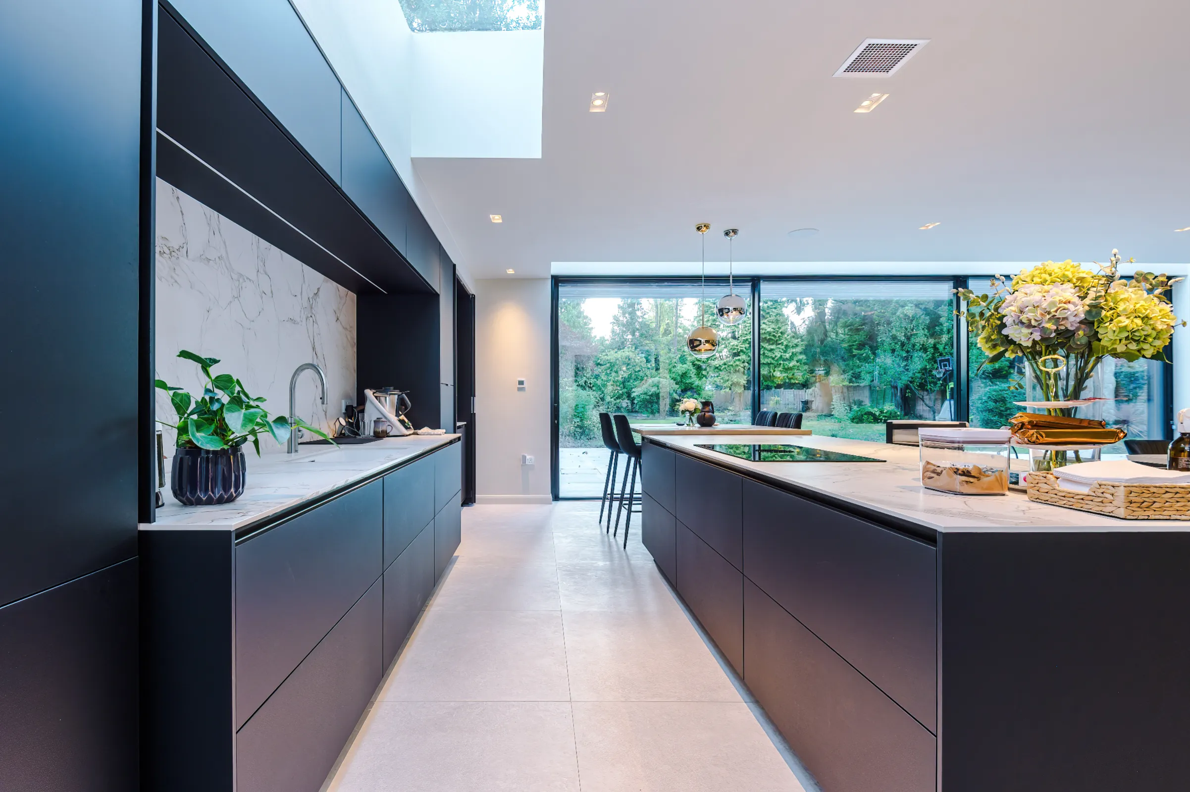 Black kitchen with central island, rooflights, and 3 panel sliding doors.