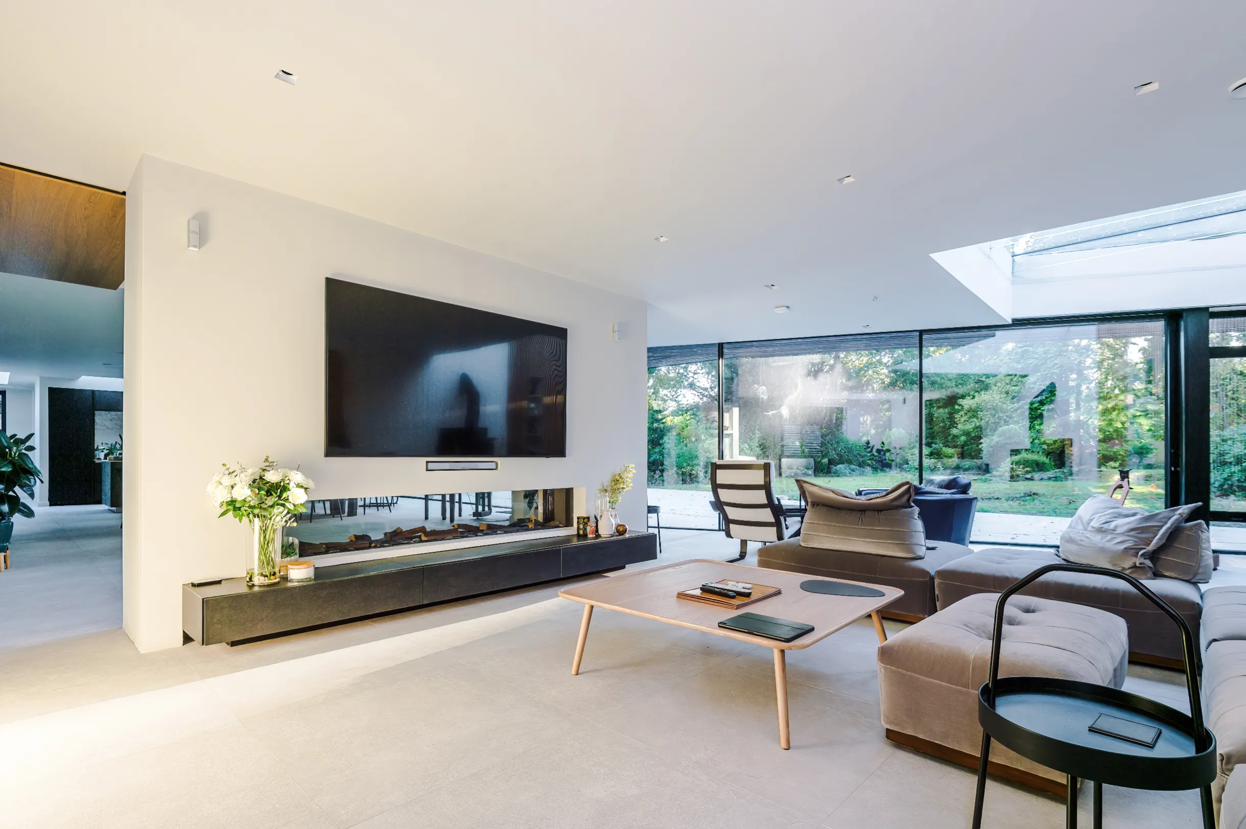 View of the multi-zone space with the lounge in the foreground and kitchen/ dining to the rear, separated by a feature wall with long fireplace and floating bench