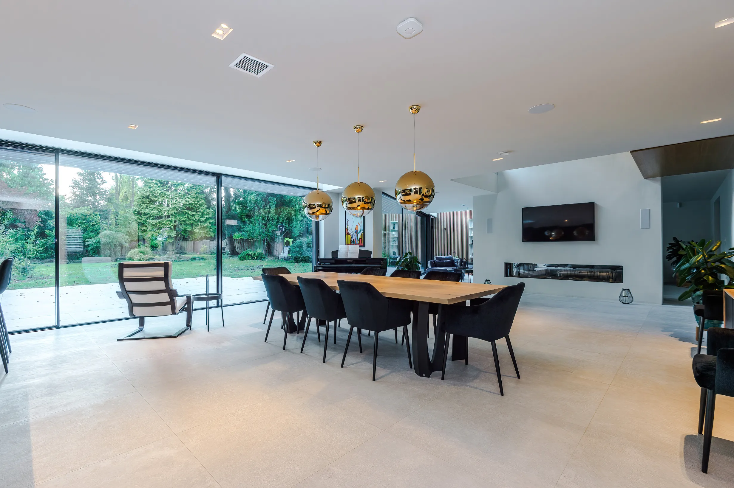 View of the multi-zone space with a feature wall separating the dining zone in foreground and the lounge at the rear, and linked to the garden by 2 sets of 3 panel, triple glazed sliding doors.