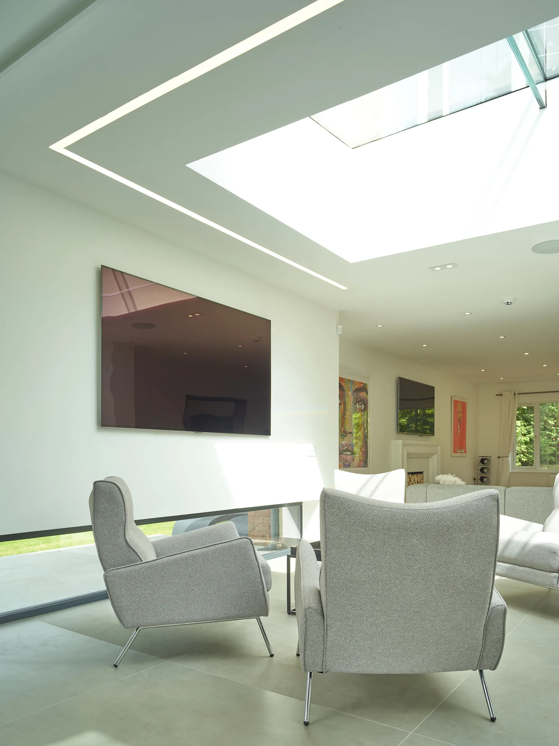 View of the ‘games’ lounge with a large rooflight above and floating wall to the side, and living room to the rear.