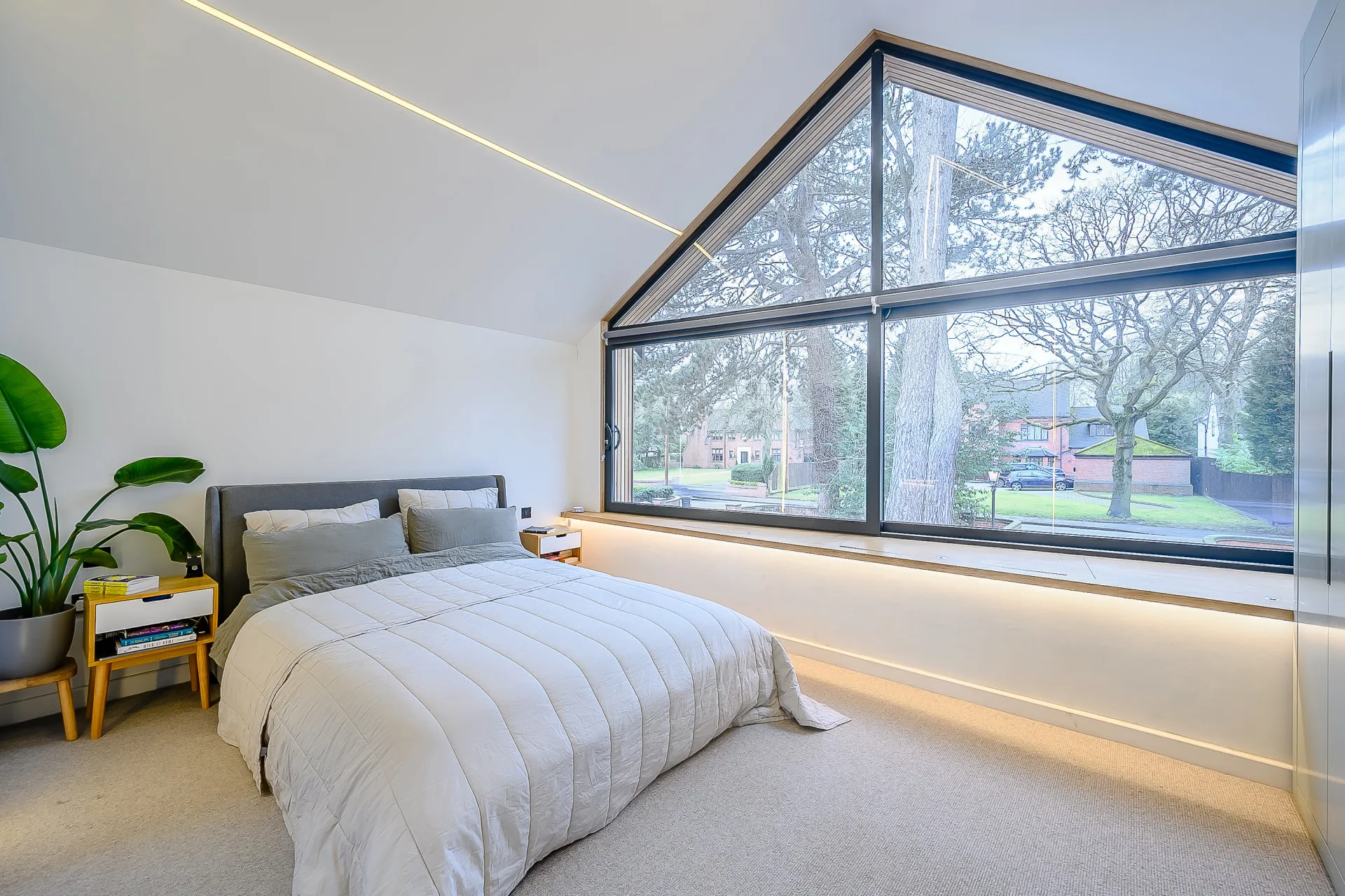 Interior view of bedroom extension over garage, featuring vaulted ceiling, window seat, strip light and sliding window.