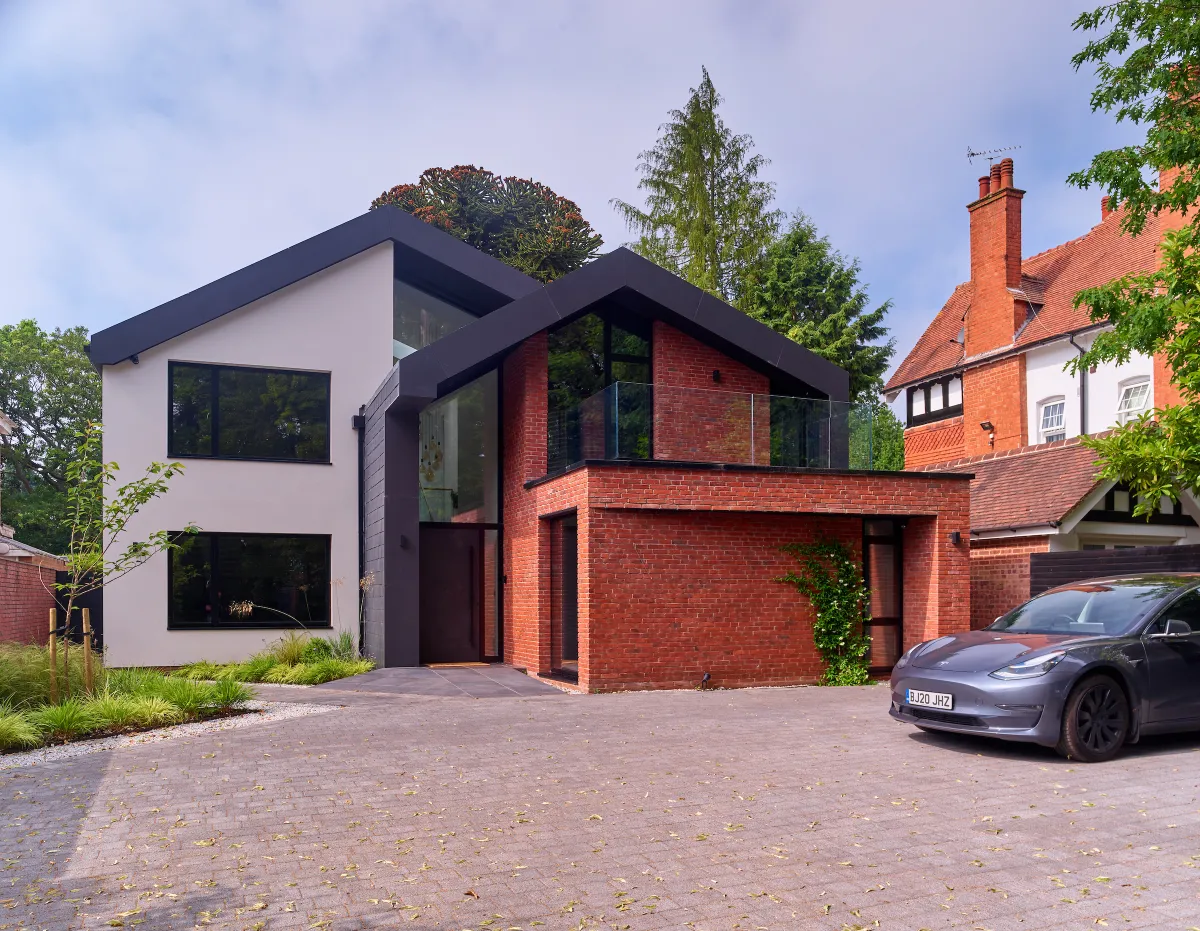 Front of dwelling double height glazed entrance feature with folding slate roof and a combination of red brick and render finishes