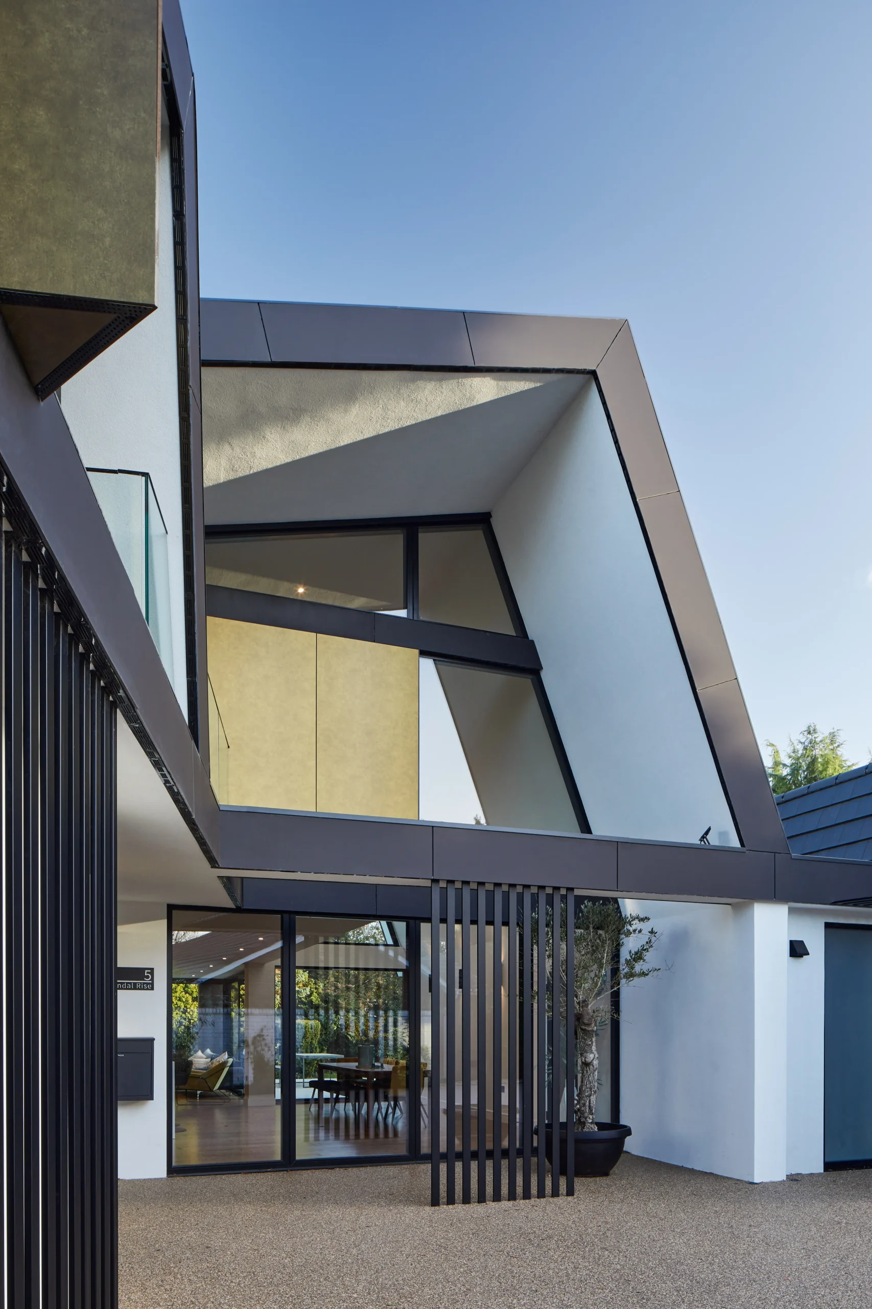 Entrance view showing angled roof forms, rendered façade, and vertical slatted screens forming a layered threshold