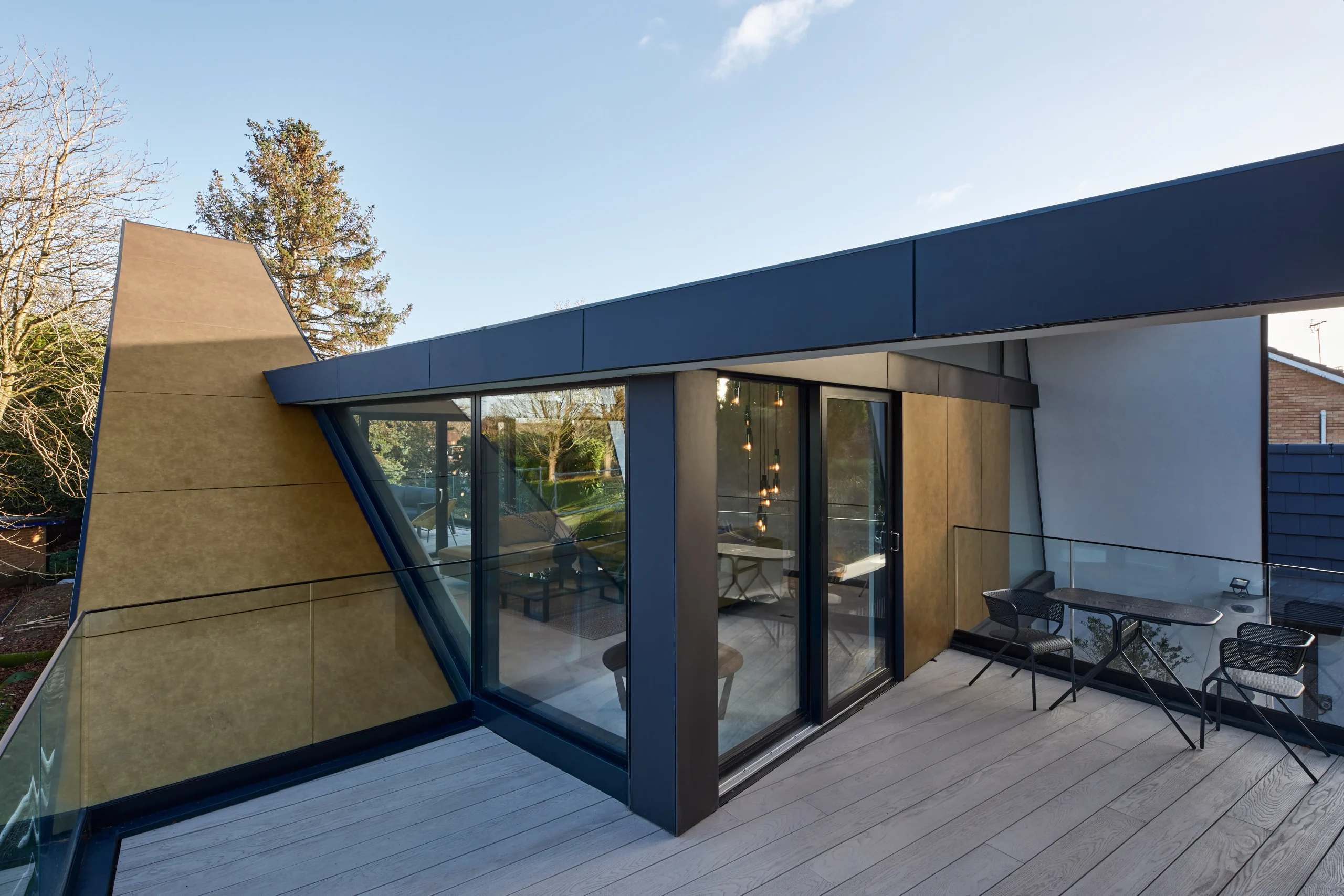 First-floor terrace showing angled corner glazing, gold-clad stair volume, and projecting roof canopy above