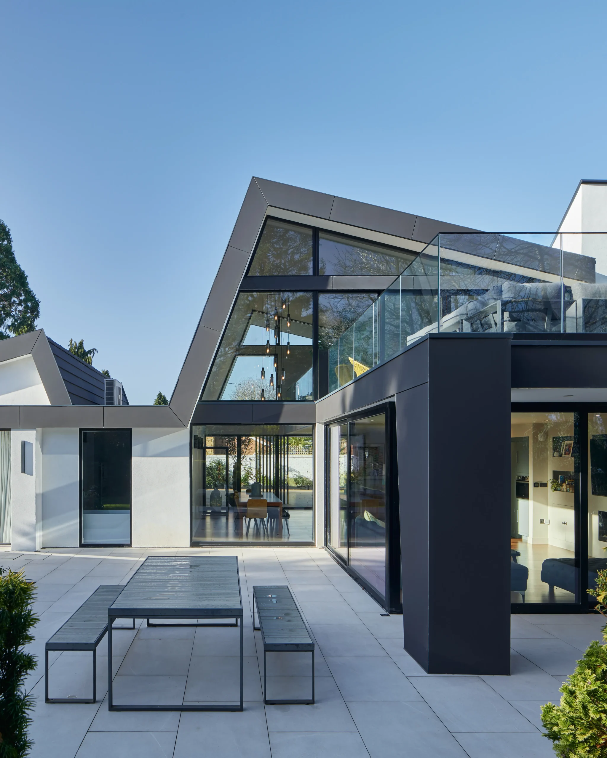 Ground-level terrace with full-height glazing to the lounge and dining space, framed by the projecting upper floor