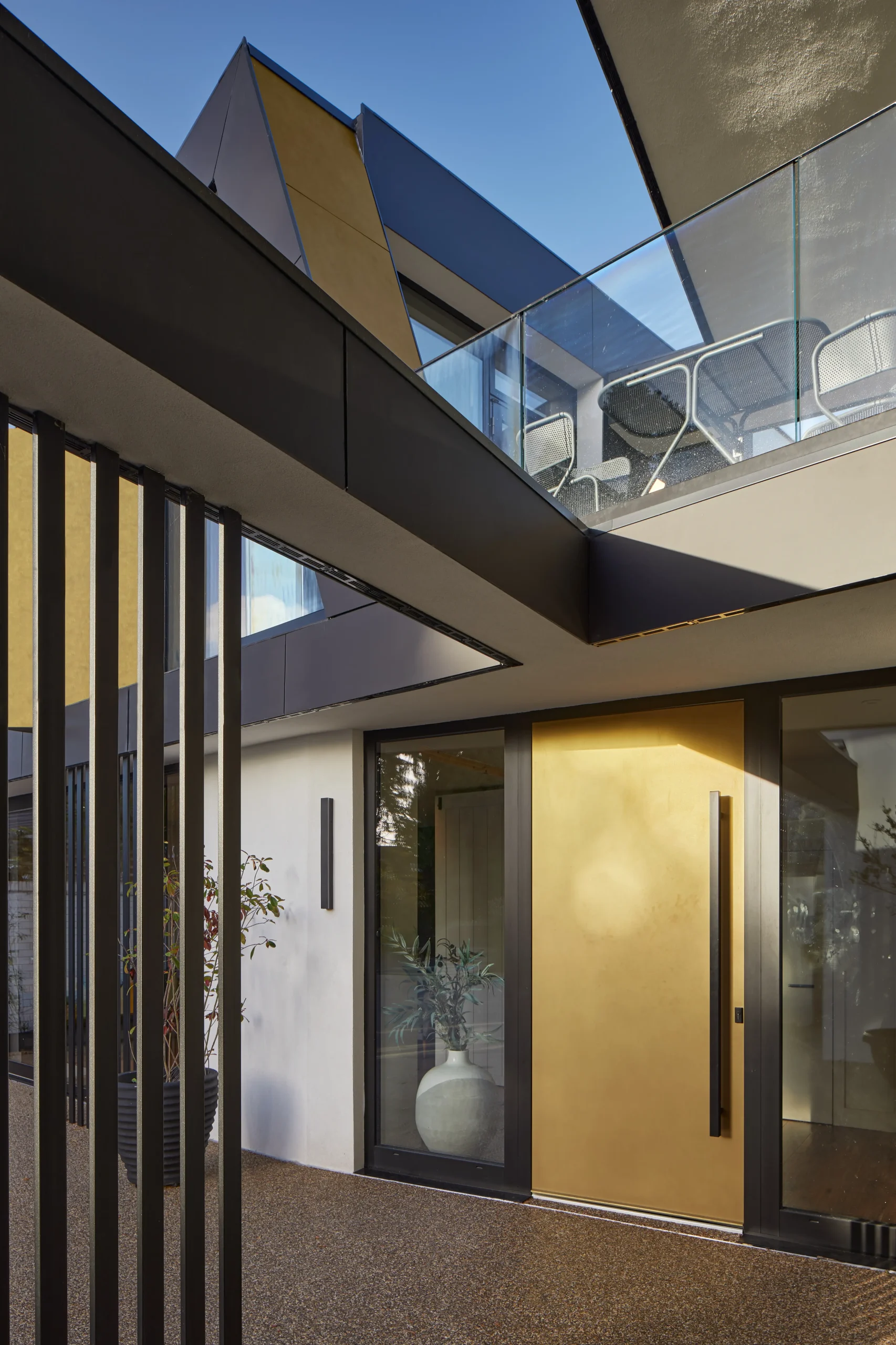 Entrance detail with gold front door, vertical screening, and upper-level terrace positioned above the arrival space