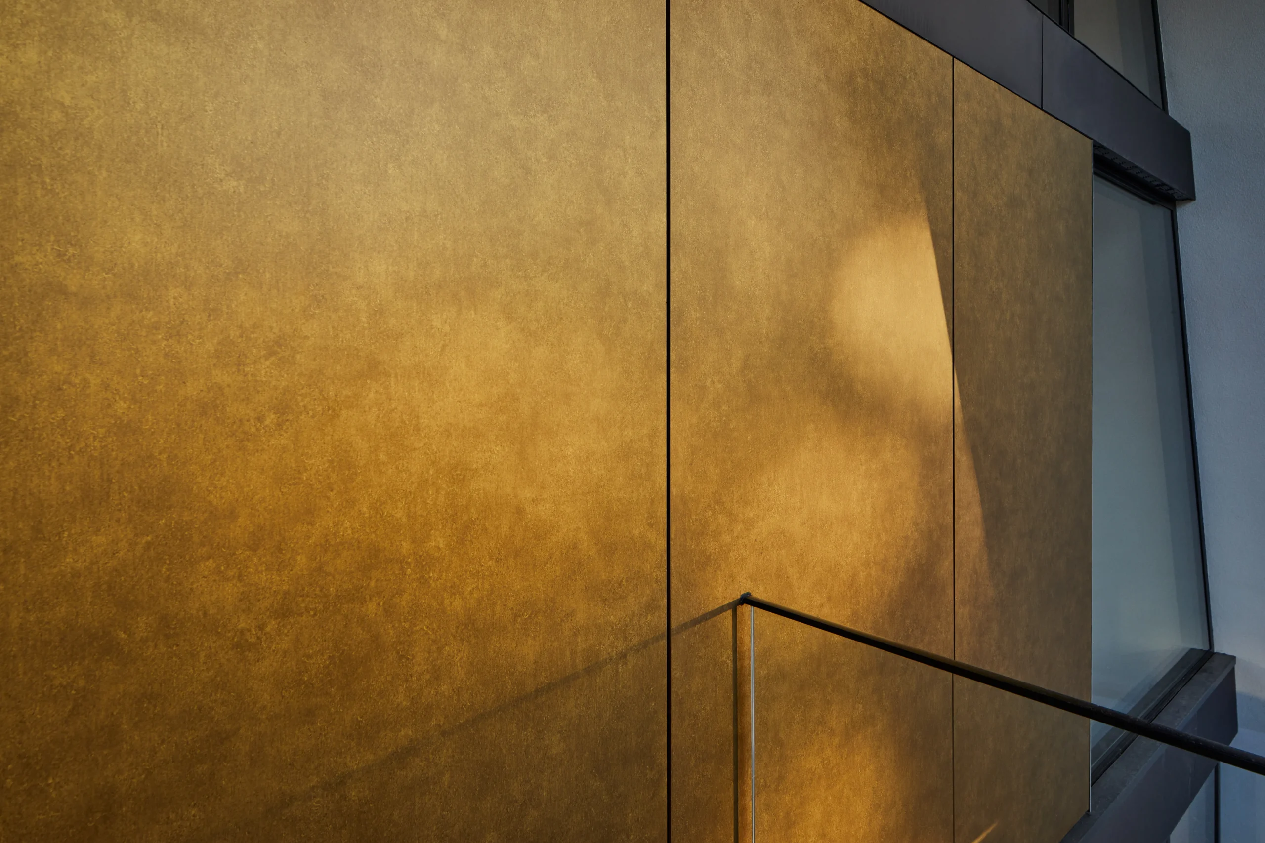 Detail of gold-coloured cladding catching reflected daylight and shadow beneath the deep roof overhang