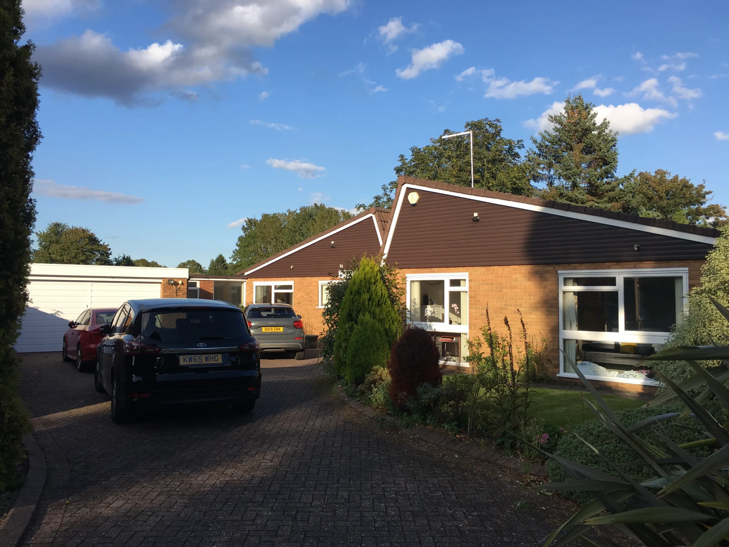 Existing street-facing view of the original single-storey house prior to refurbishment, with brick façades, pitched roofs and driveway parking.