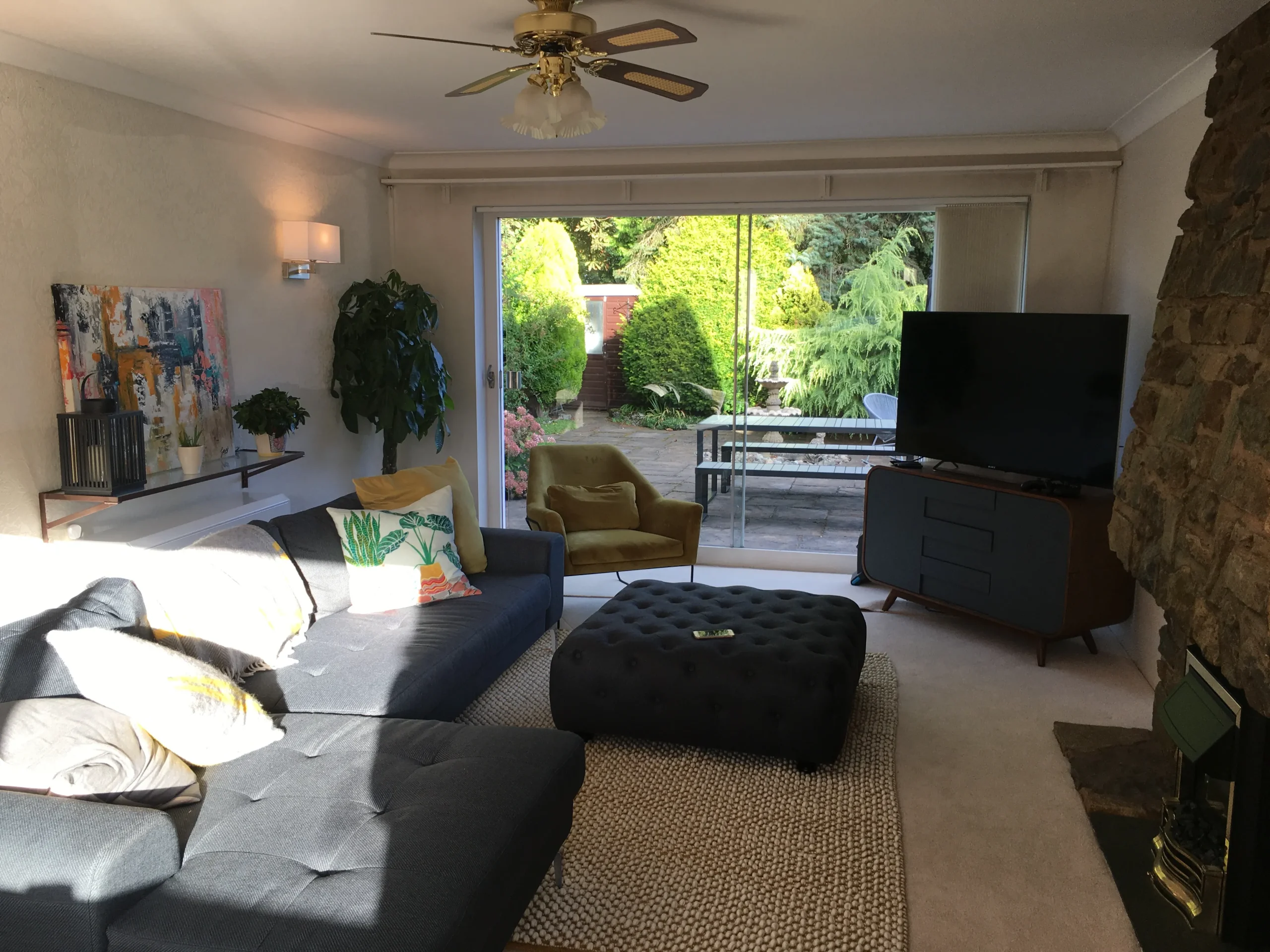 Existing interior lounge prior to remodelling, with low ceiling, stone fireplace, ceiling fan and sliding doors opening onto the rear garden.